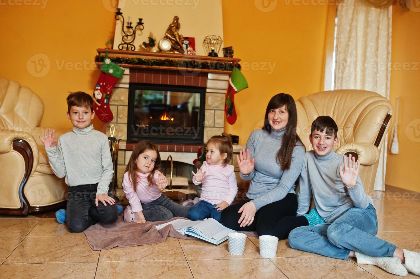 Happy young large family by a fireplace in warm living room on winter day. Mother with four kids at home. photo