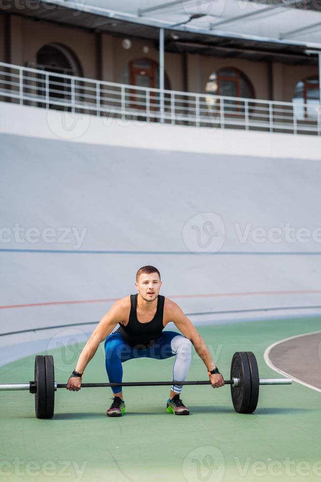 Young guy raises the bar in the stadium, outdoor workout photo