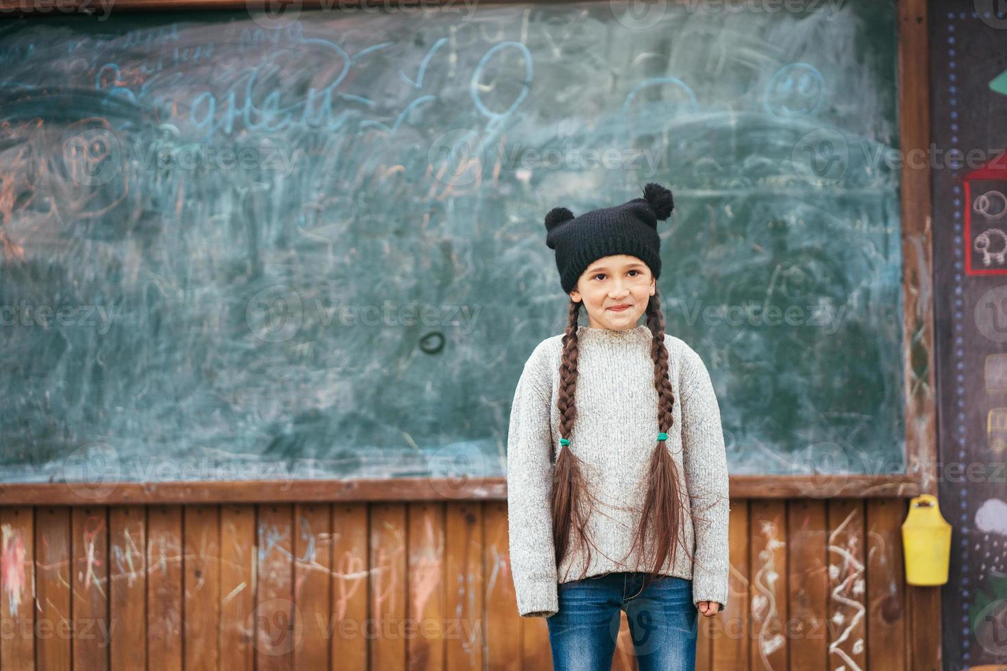 Little girl in a hat posing on the background of the school blackboard photo