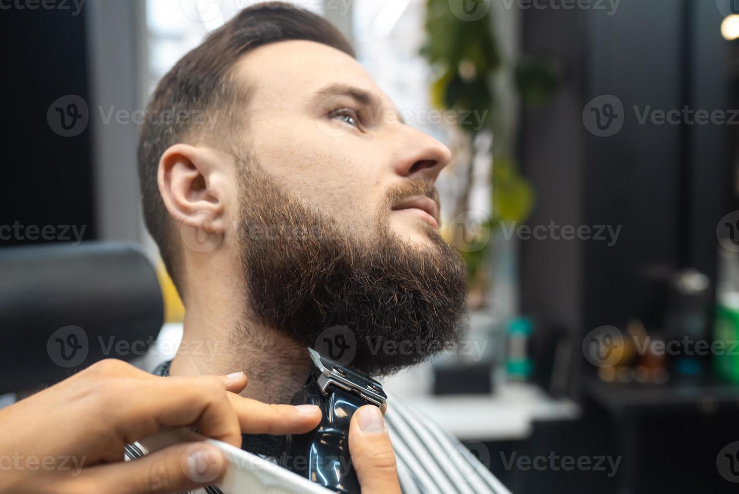 Barber works with a beard clipper. Hipster client getting haircut. photo