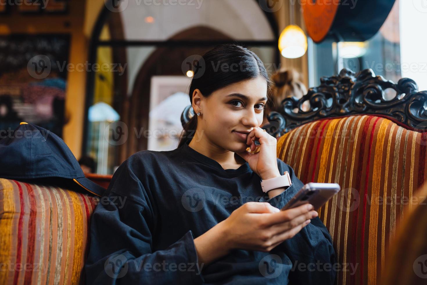 una joven guapa descansando en una gran silla blanda en un café, charlando por teléfono foto