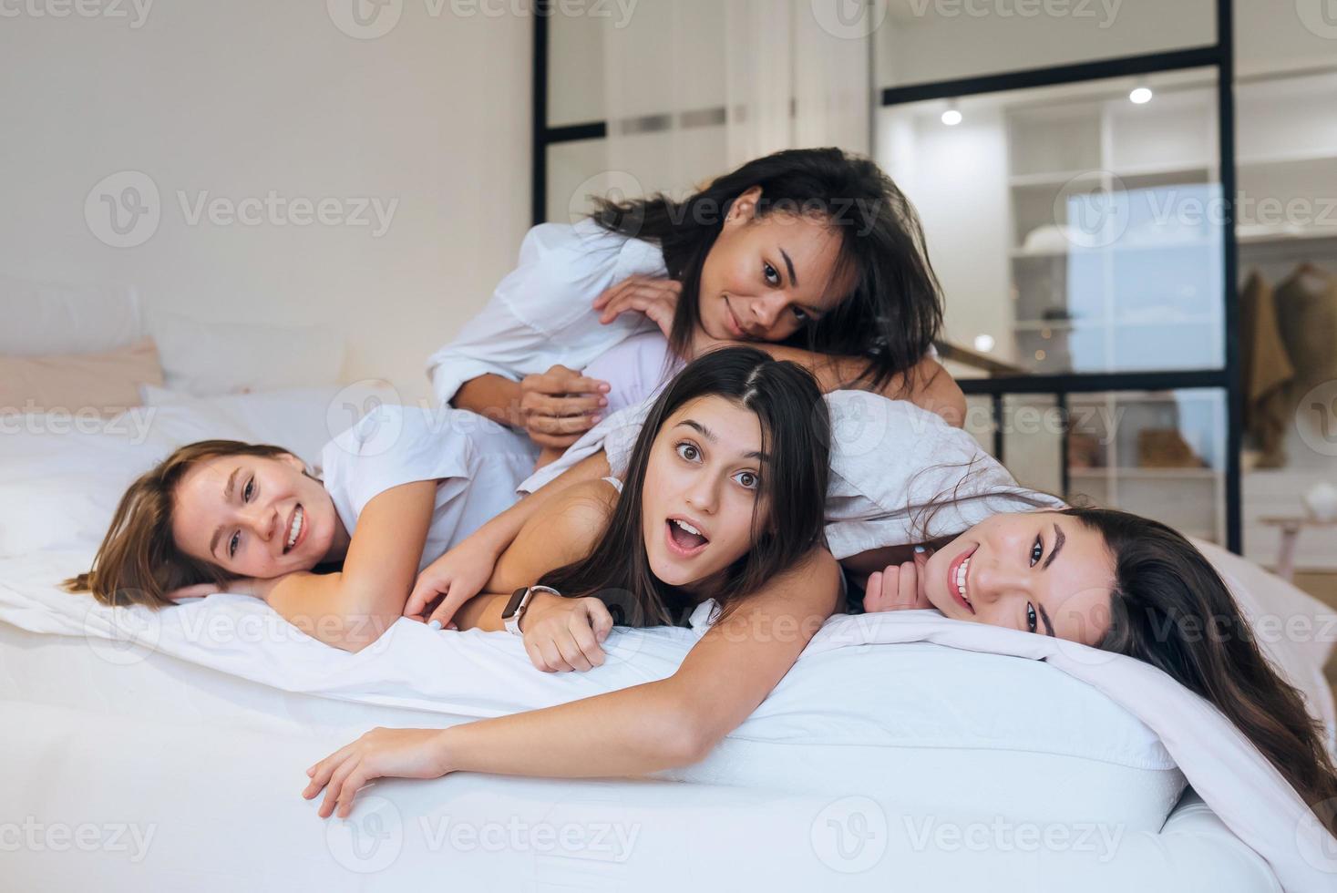 Positive young girls women friends indoors on bed at the hen party at home. photo