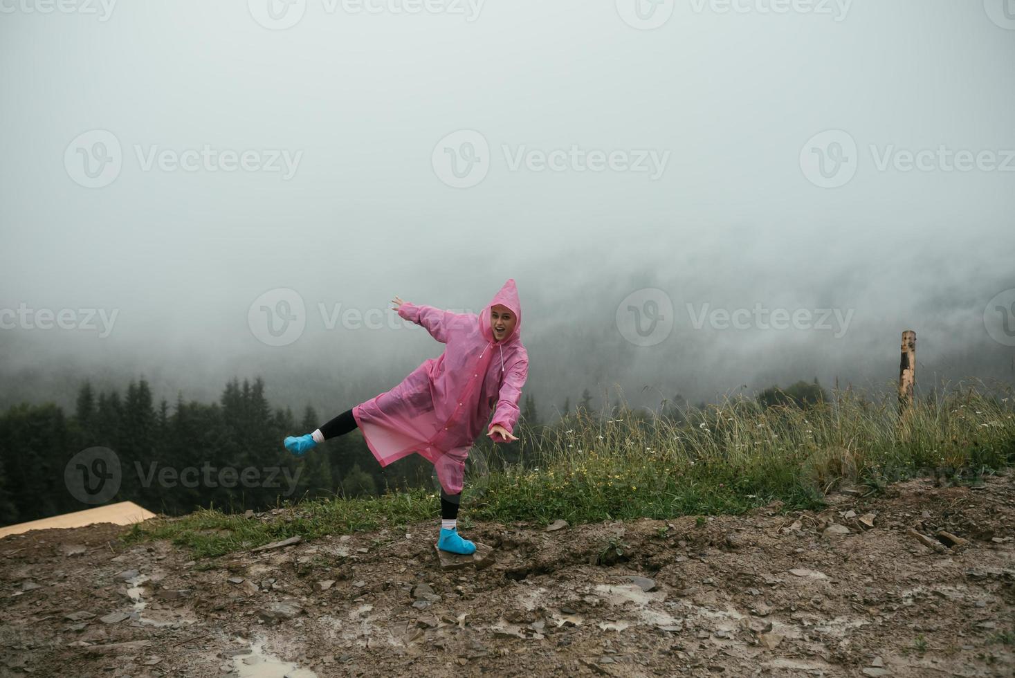 Attractive hiker girl in a pink raincoat stands on a mountain photo