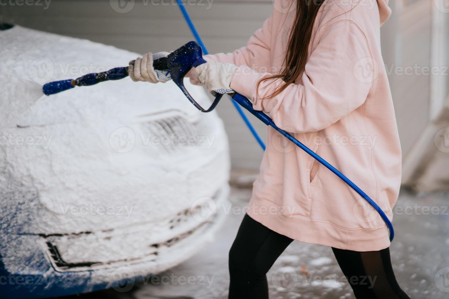 Brunette from a high-pressure hose applies a cleaner on the car photo