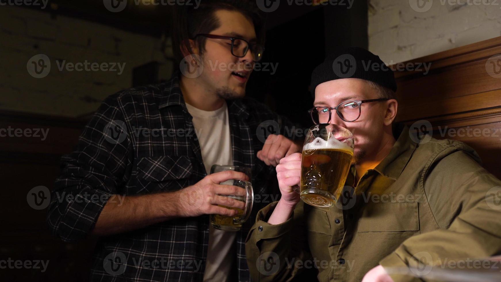 jóvenes amigos divirtiéndose juntos bebiendo cerveza y tintineando vasos en un pub. foto