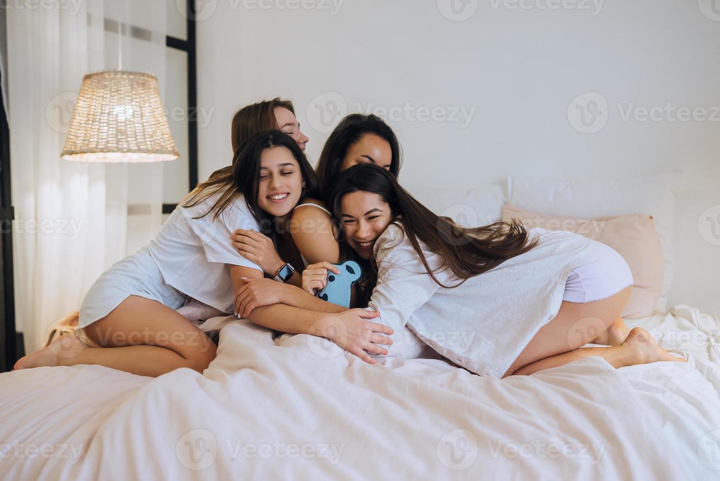 Positive young girls women friends indoors on bed at the hen party at home. photo