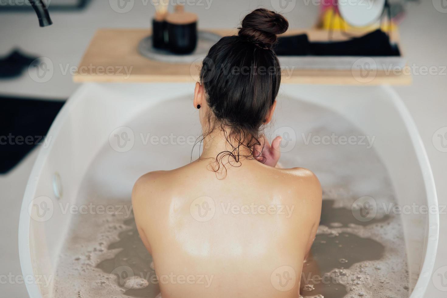 mujer joven abrazándose tomando un baño vista desde atrás foto