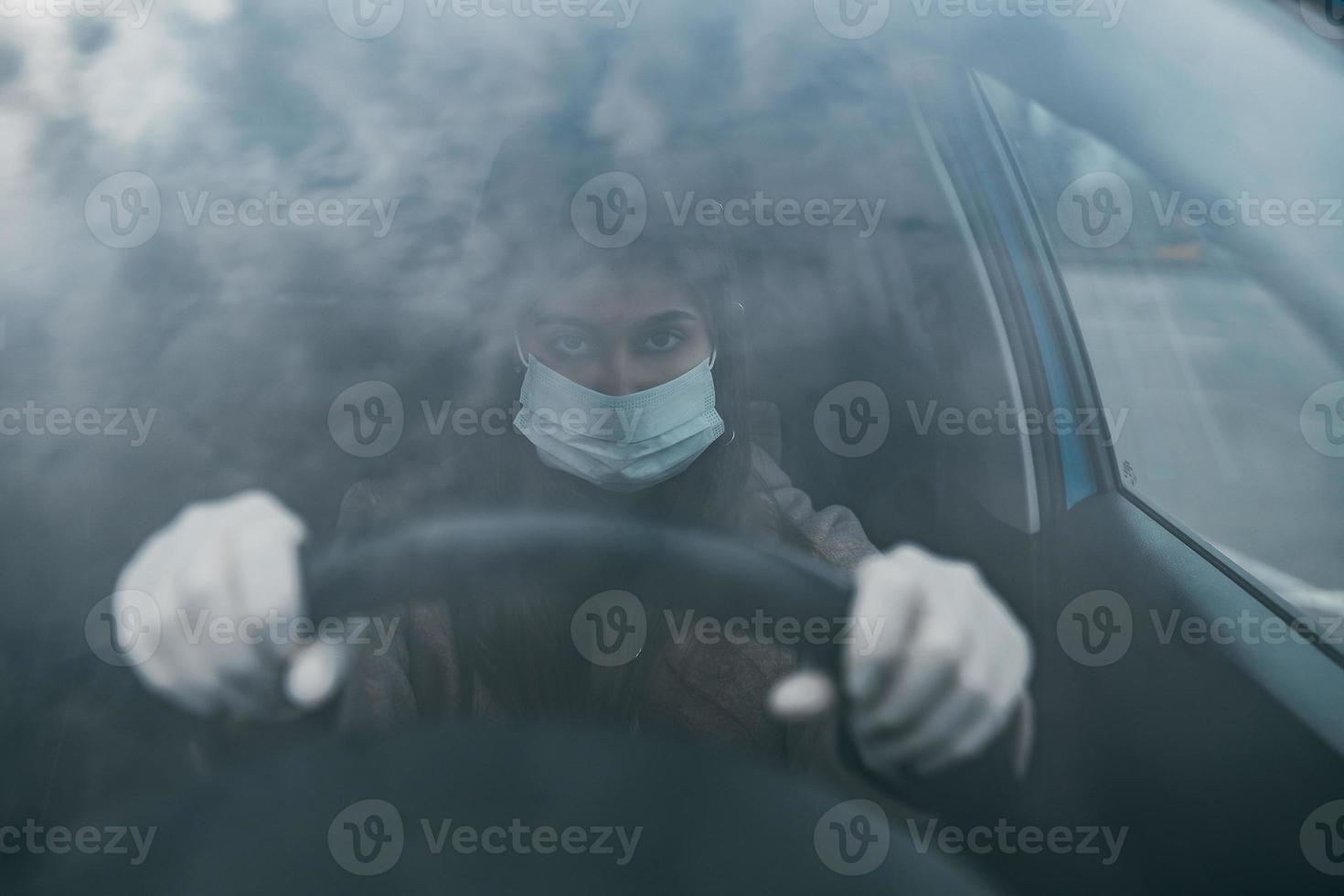 Young woman in a mask and gloves driving a car. photo