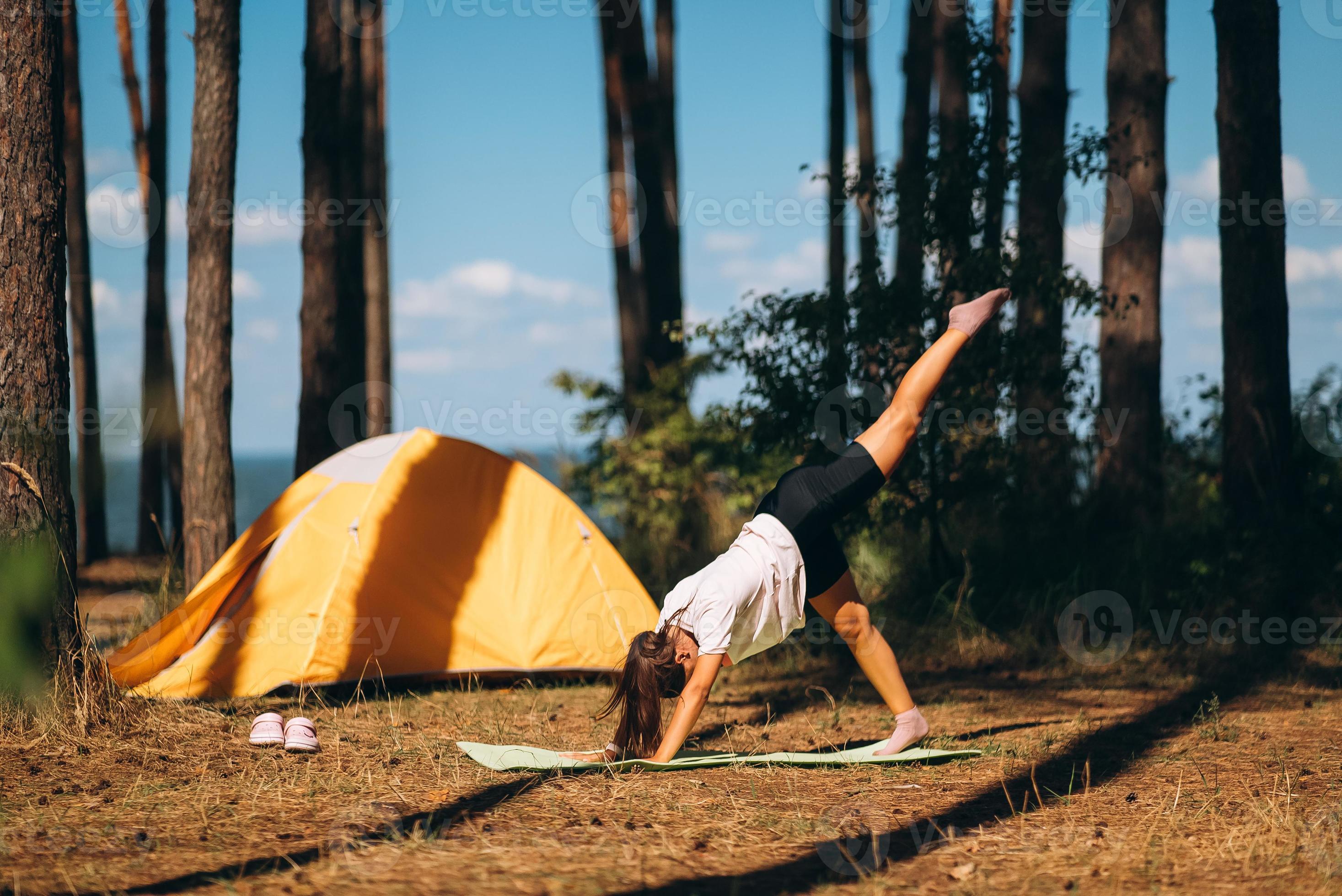 Woman doing morning yoga exercises in woods near yellow tourist