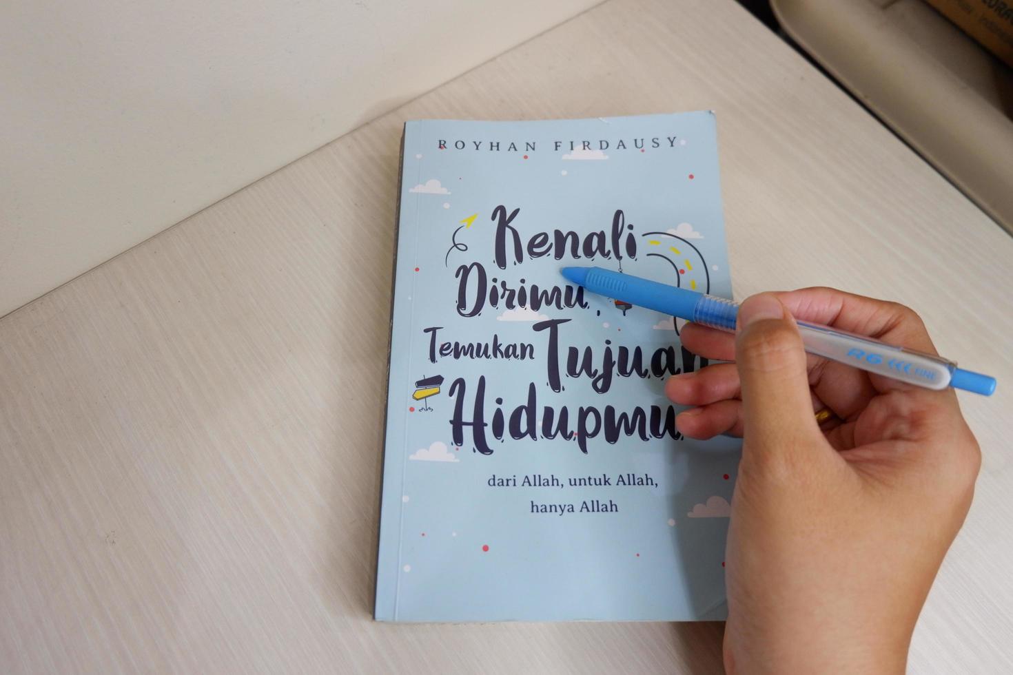 Jakarta, Indonesia - April, 17, 2021, The hand holding the pen is pointing at the book that is on the table photo