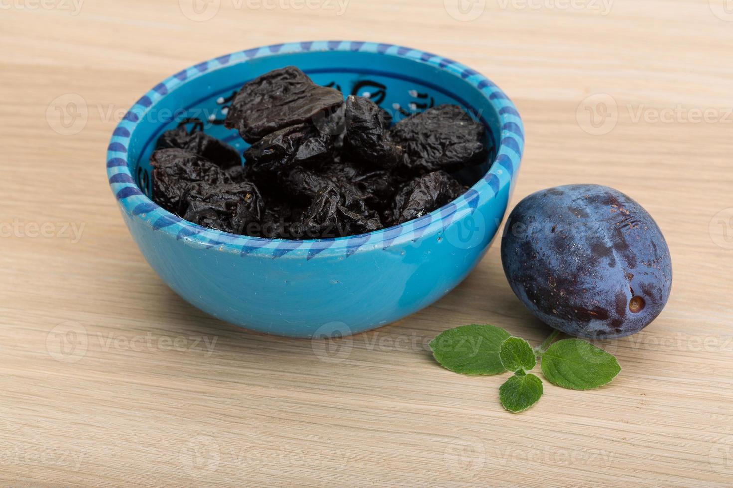 Dried plums in a bowl on wooden background photo