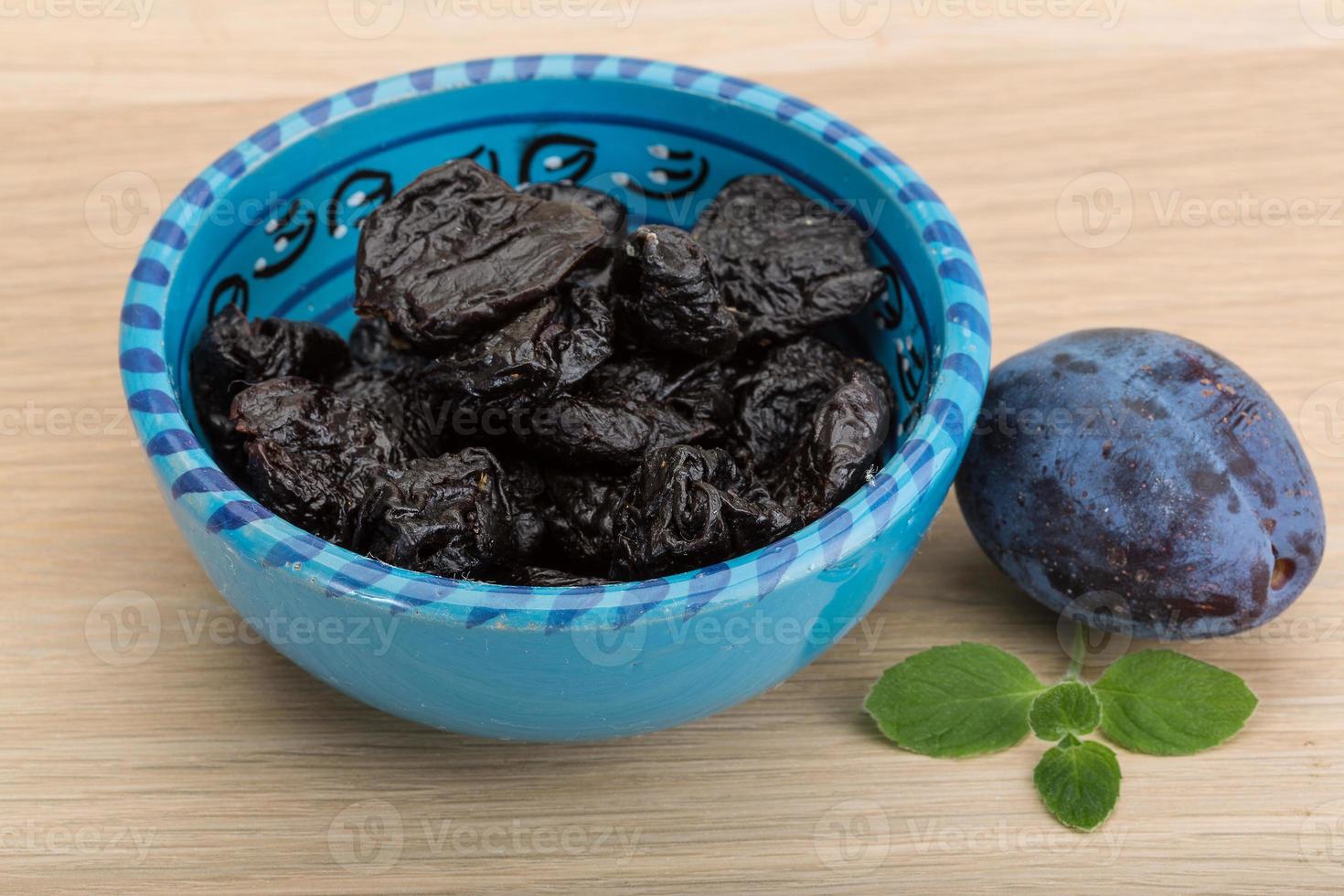 Dried plums in a bowl on wooden background photo