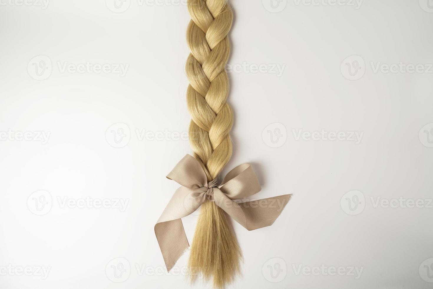 A blonde tress with a beige bow lying on a white background photo