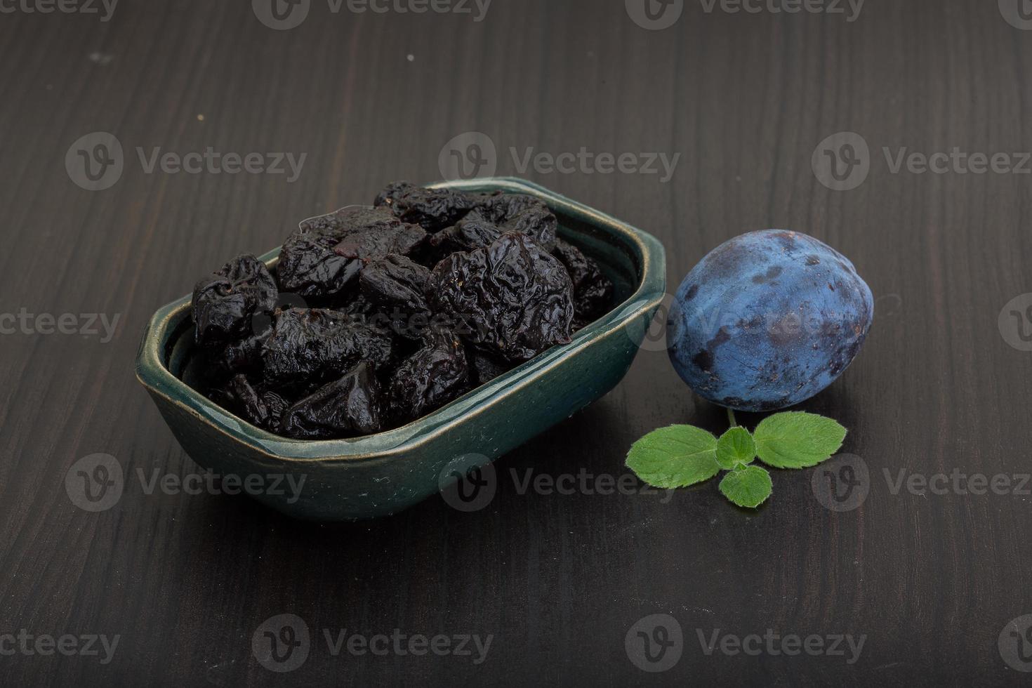 Dried plums in a bowl on wooden background photo