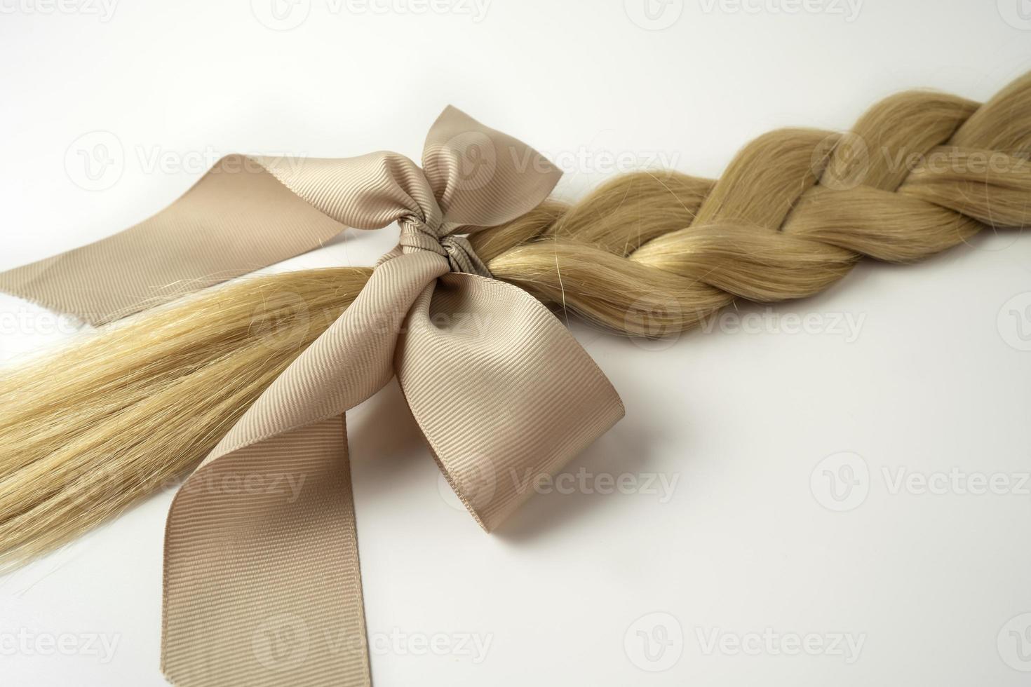 A blonde tress with a beige bow lying on a white background photo