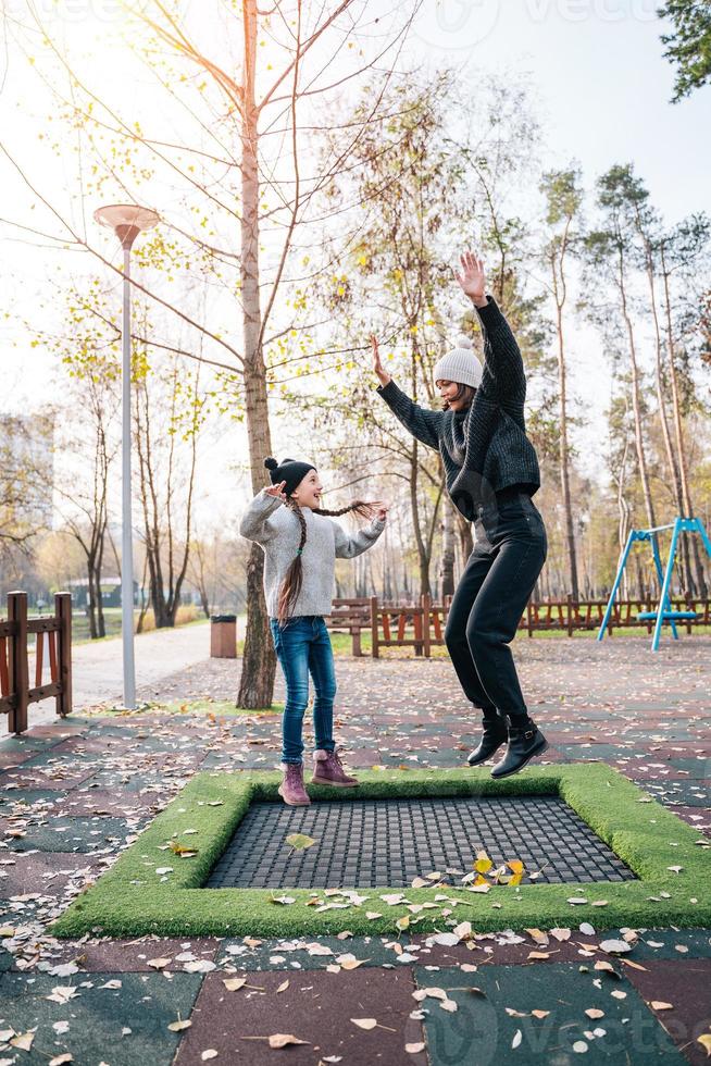 Mom and her daughter jumping together on trampoline in autumn park photo