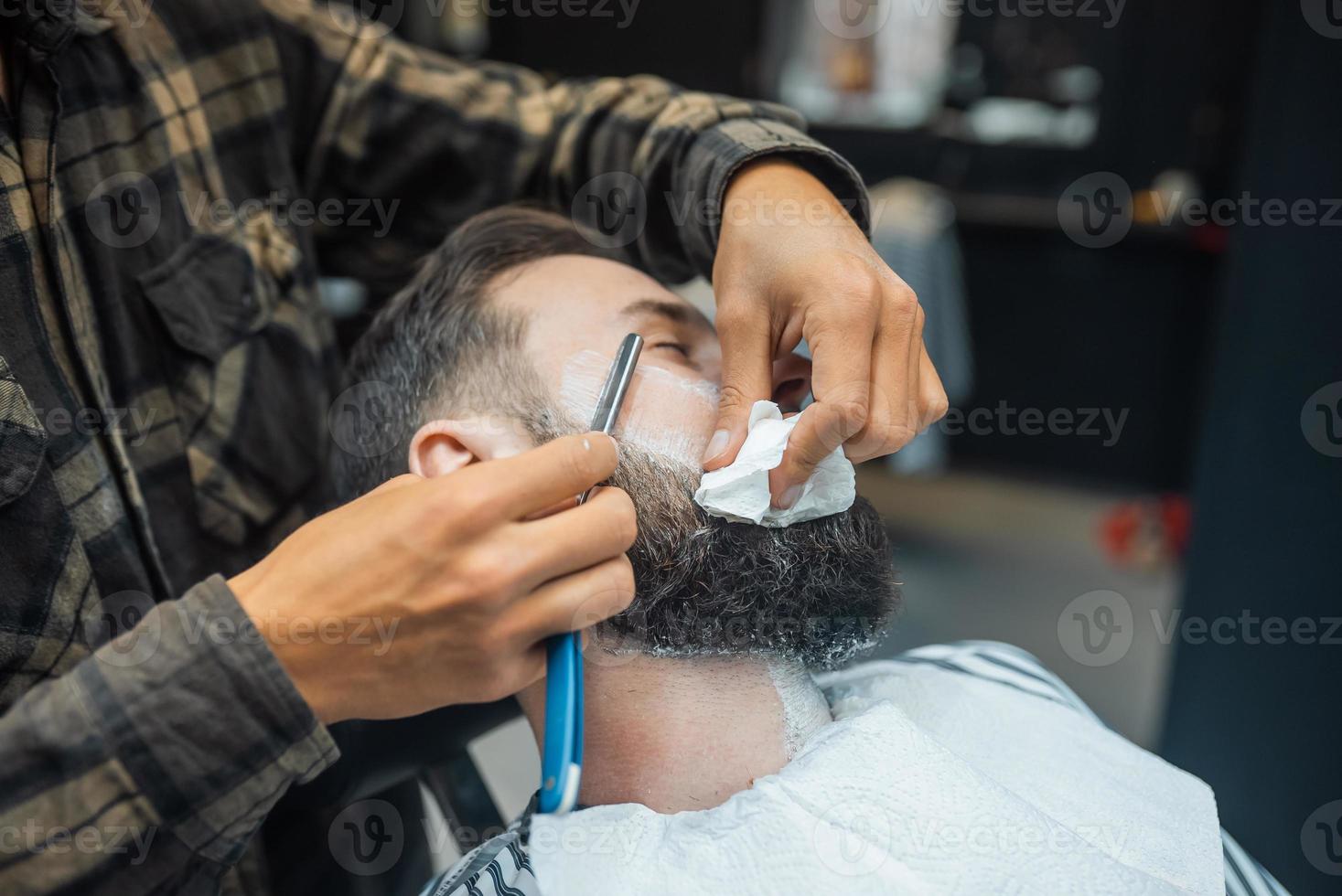 joven barbudo siendo afeitado por el peluquero en la barbería foto