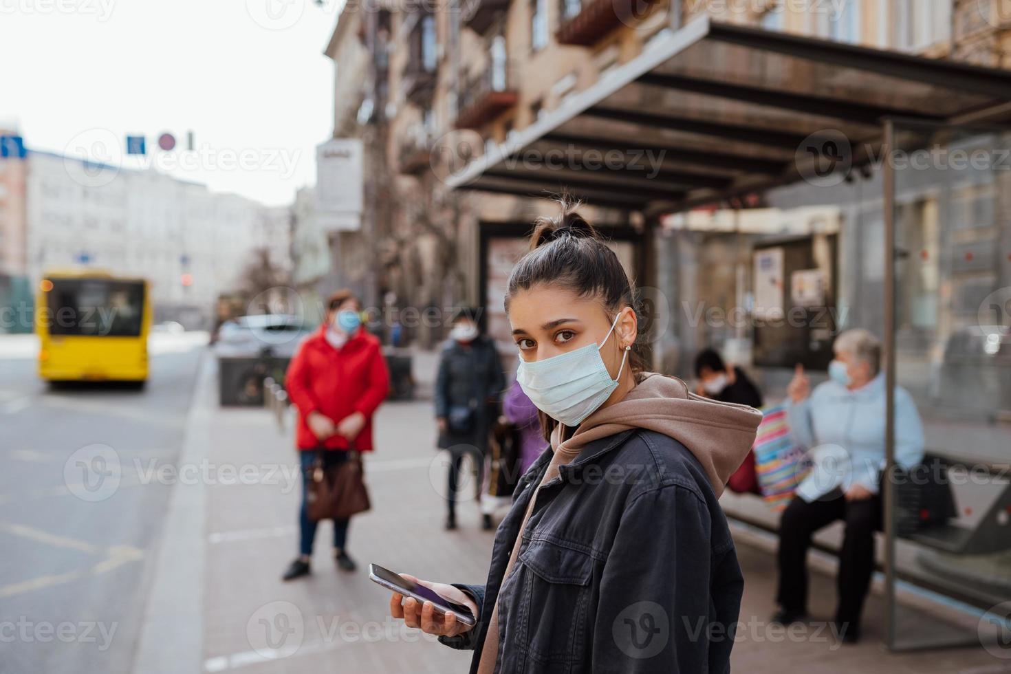 Young woman wearing surgical mask outdoor at bus stop in the street photo