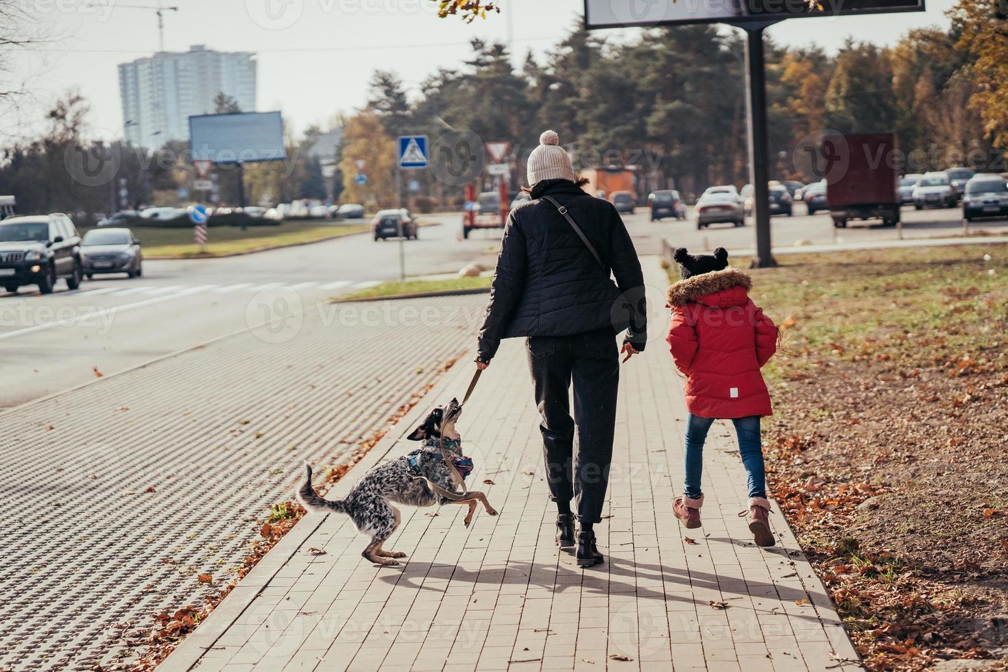 Happy mother and her daughter walk with dog at the street. photo