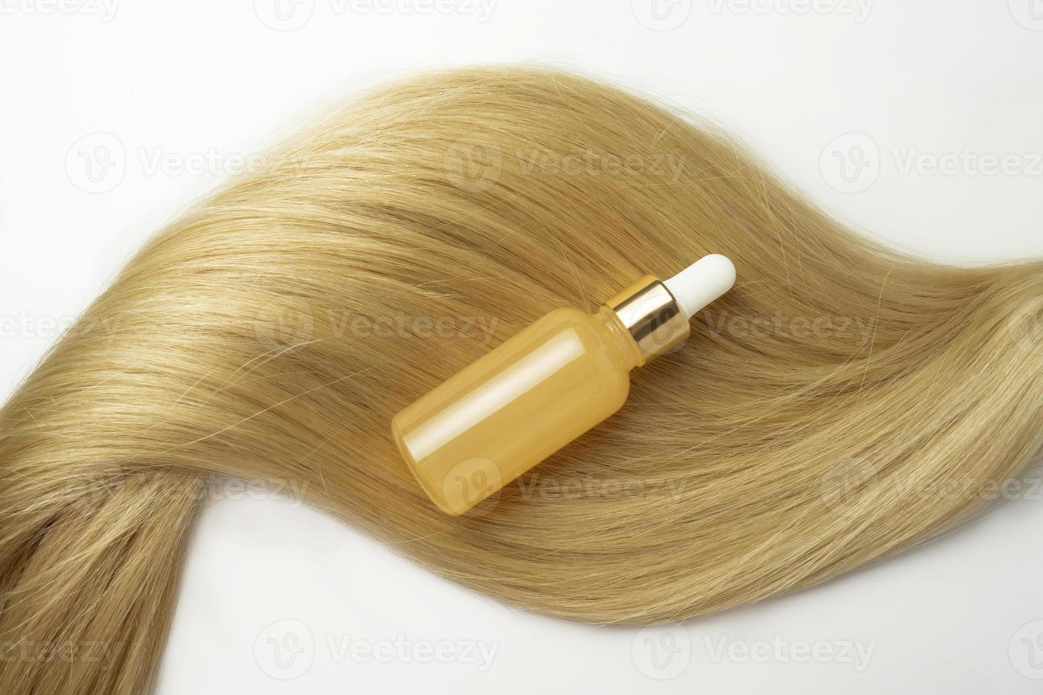 A blonde tress with a natural oil or serum for hair care lying on it photo