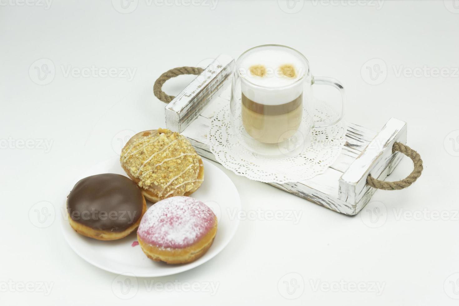 A cup of latte stands on a wooden tray for early breakfast and sweet glazed donuts photo