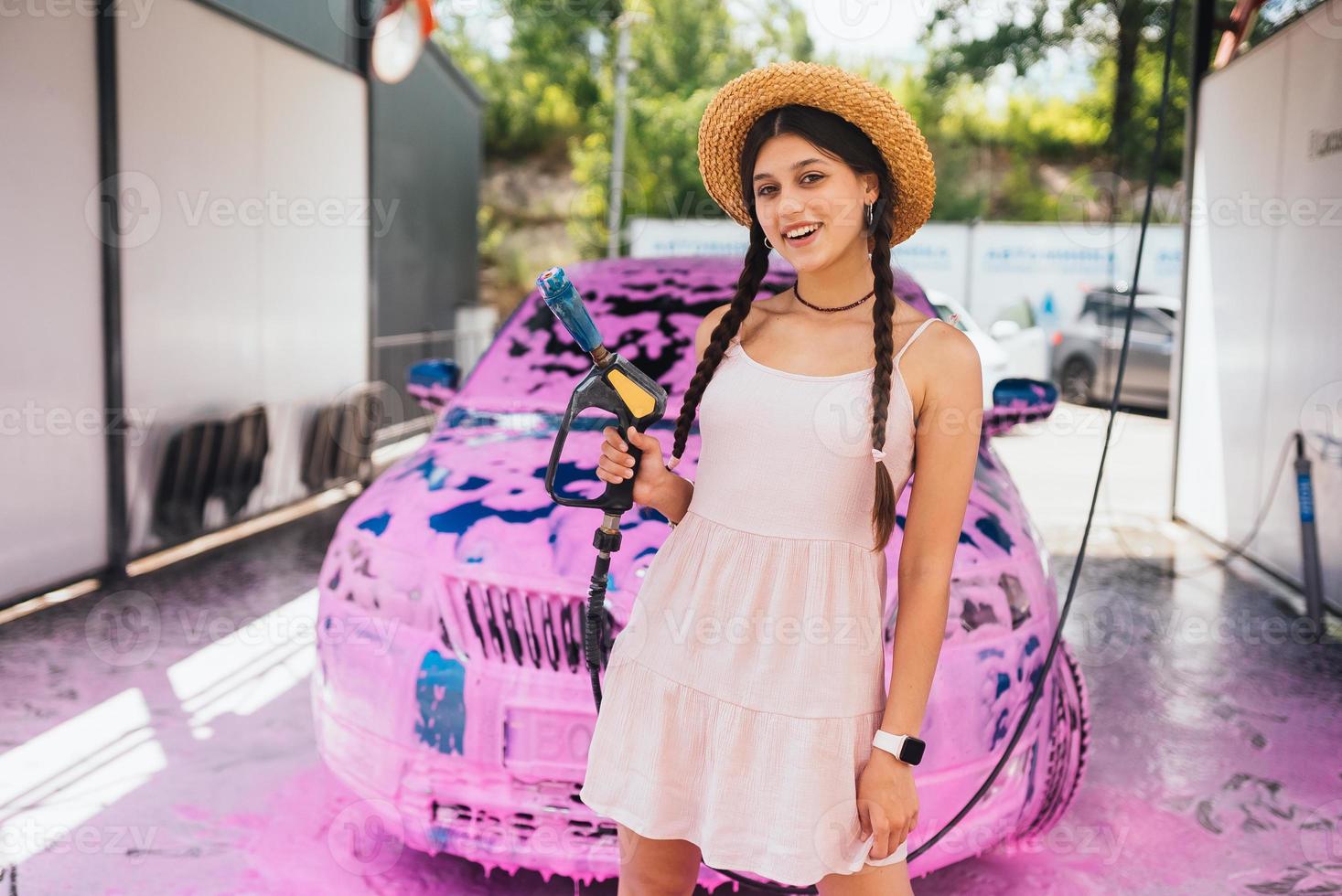 manguera de mujer joven se para frente a un camión cubierto de espuma rosa foto