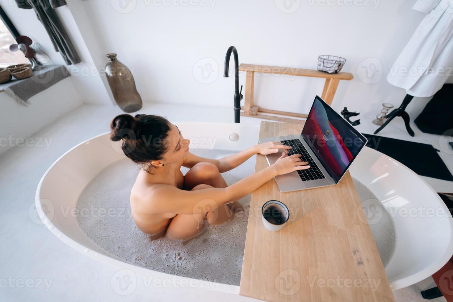 Young woman working on laptop while taking a bathtub photo