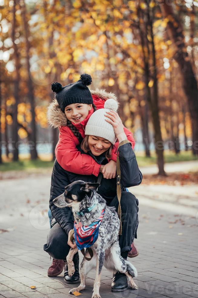 Happy mother and her daughter playing with dog in autumn park photo