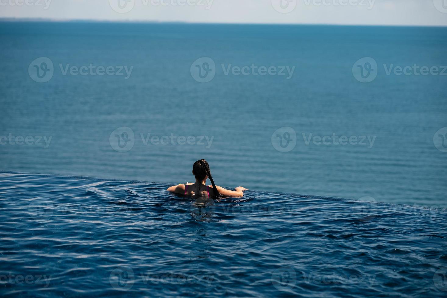 mujer feliz en traje de baño nadando en la piscina infinita frente al mar. foto