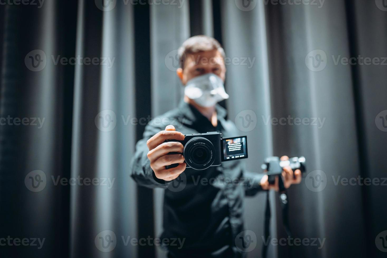 Close-up portrait of a guy holding in hands camera wearing safety mask photo
