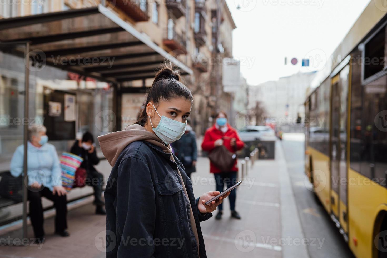 Young woman wearing surgical mask outdoor at bus stop in the street photo