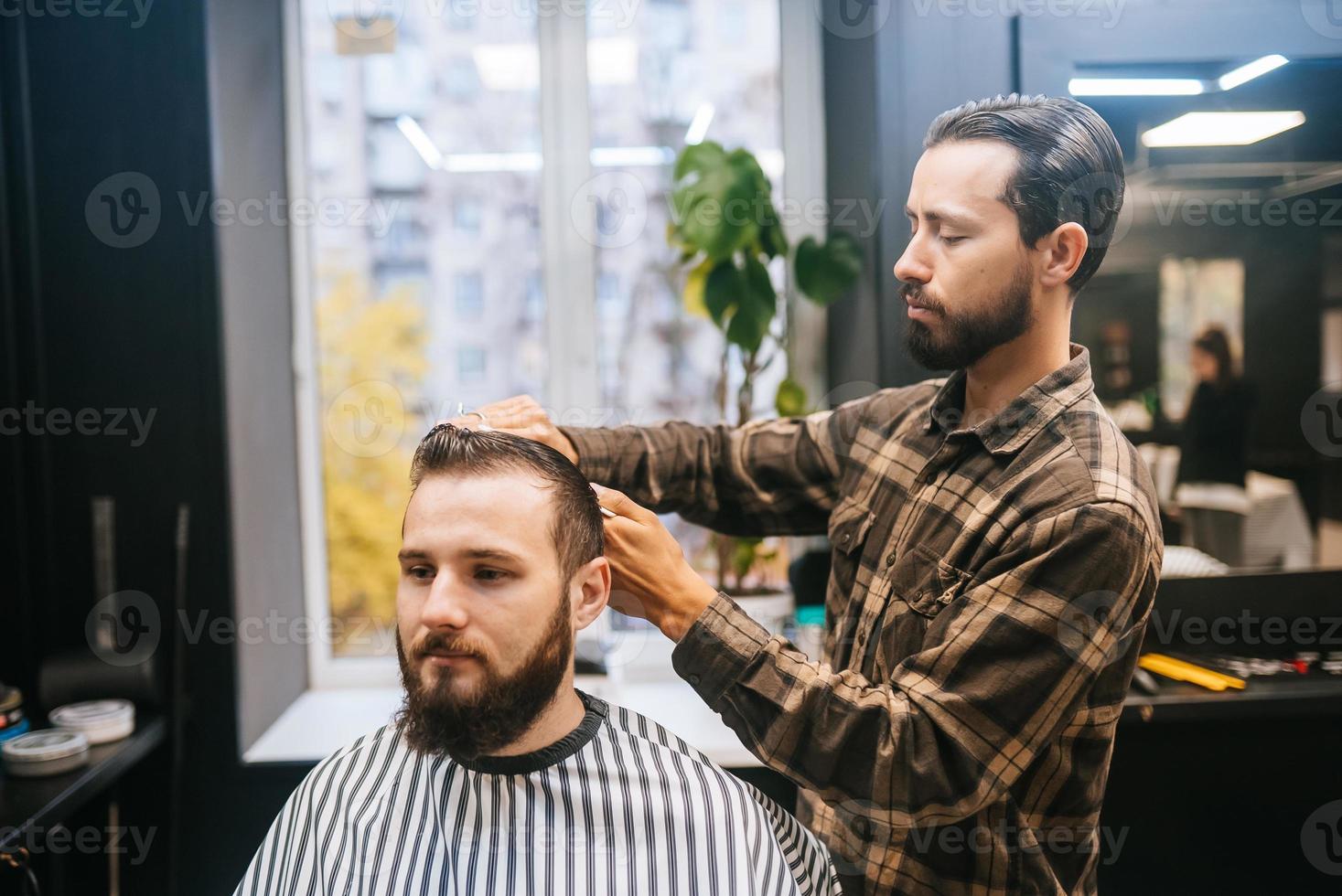 alegre joven barbudo cortándose el pelo por el peluquero en la barbería foto