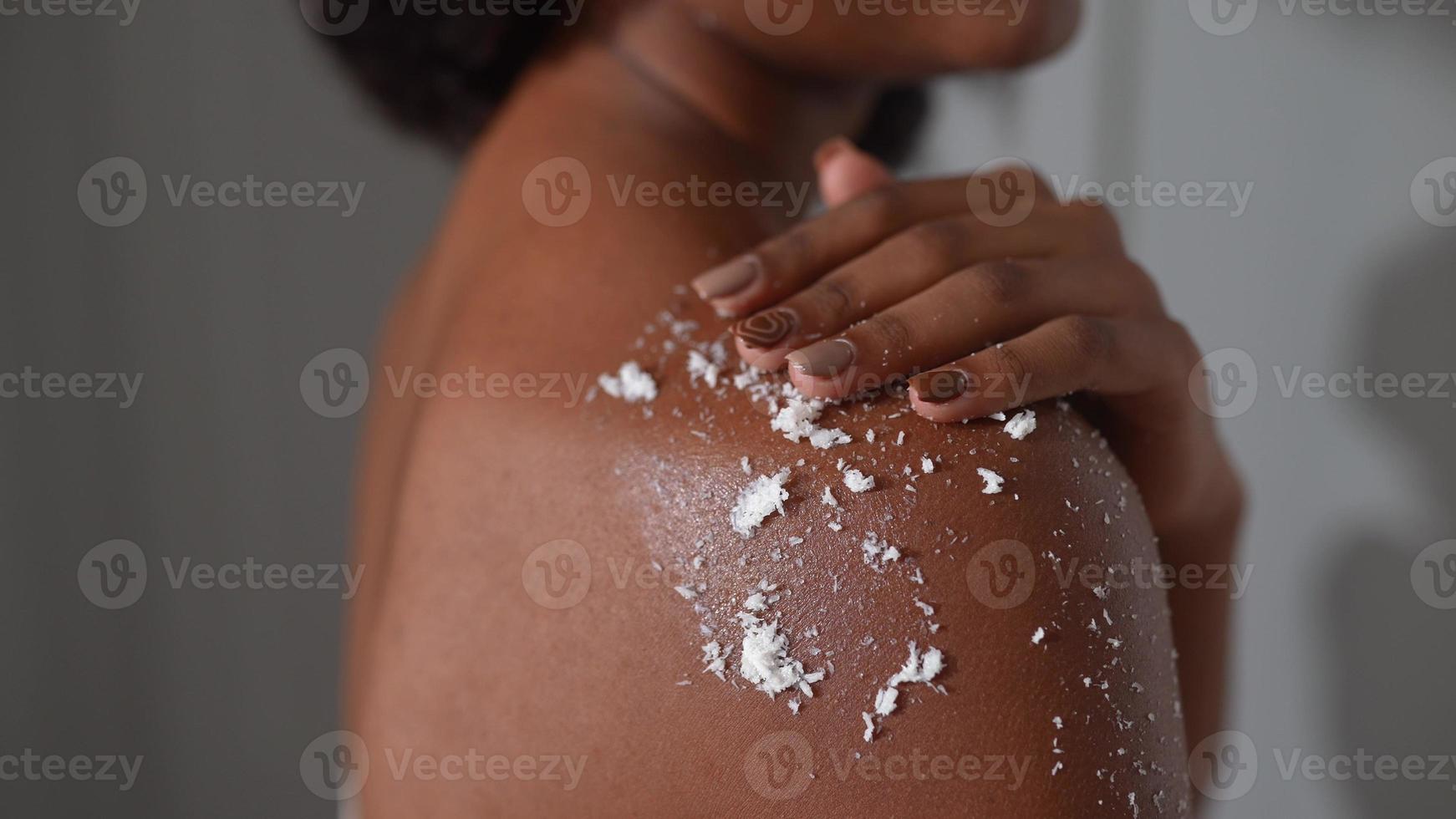 African american woman rubs scrub on shoulder skin in bathroom photo