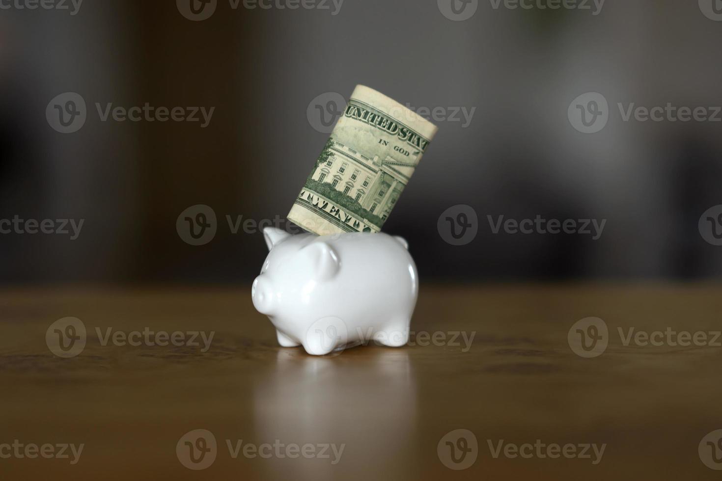 A white piggybank with a dollar banknote in it stands on the table photo