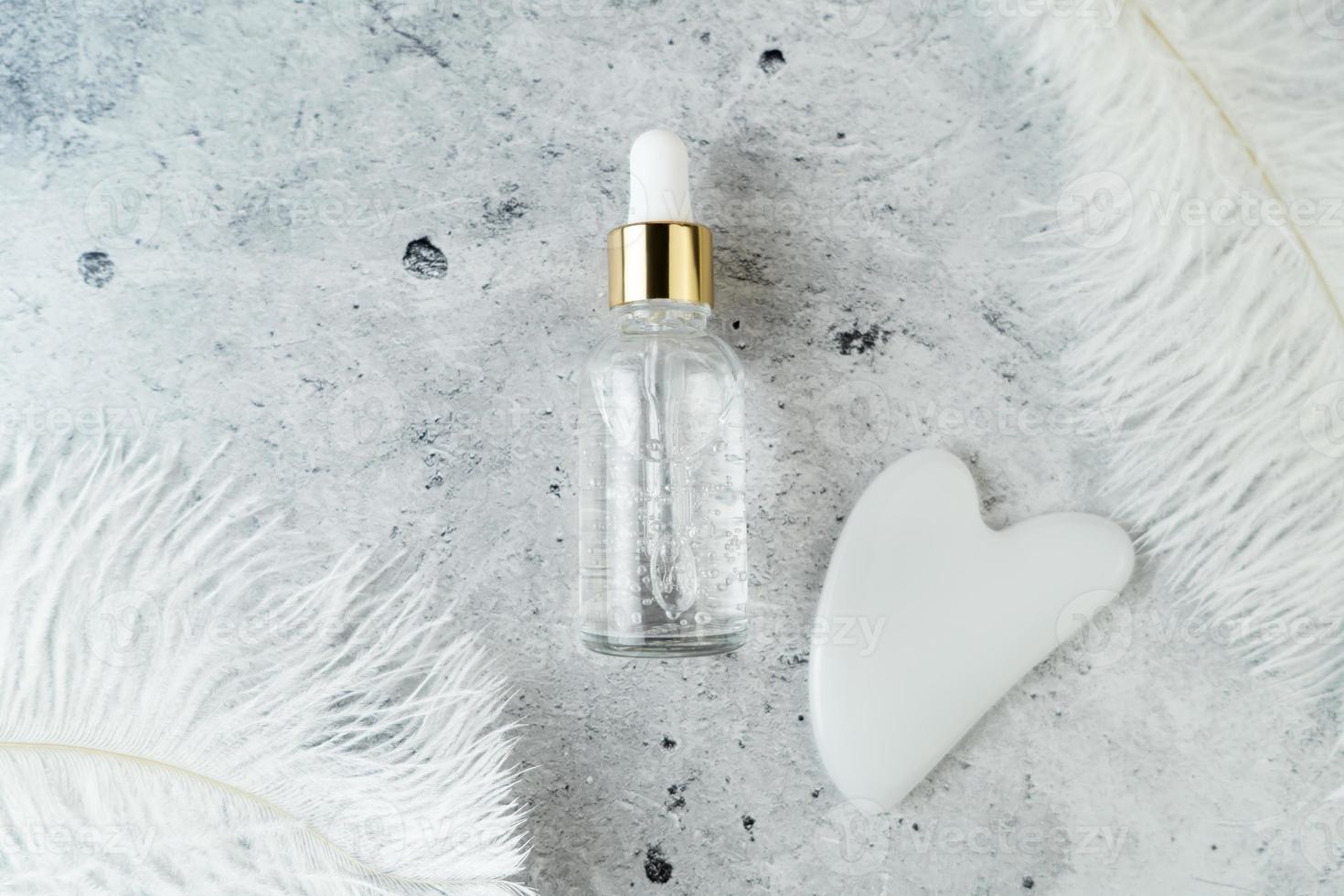 A white Guasha face massager and a face serum lying on a grey background photo