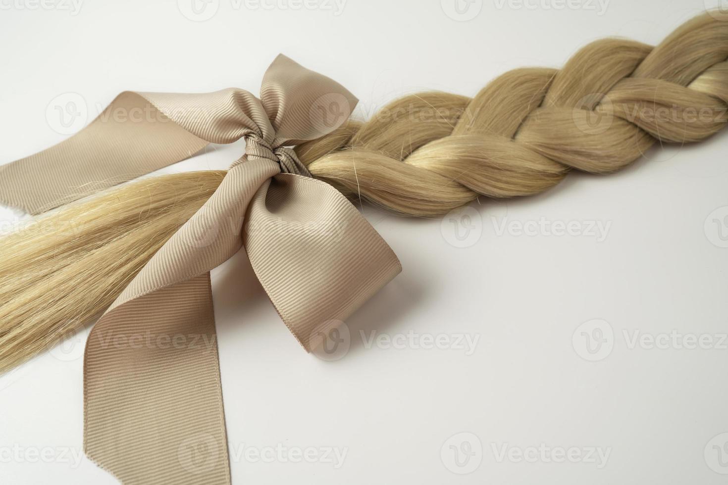 A blond hair tress with a beige bow lying on a white background photo