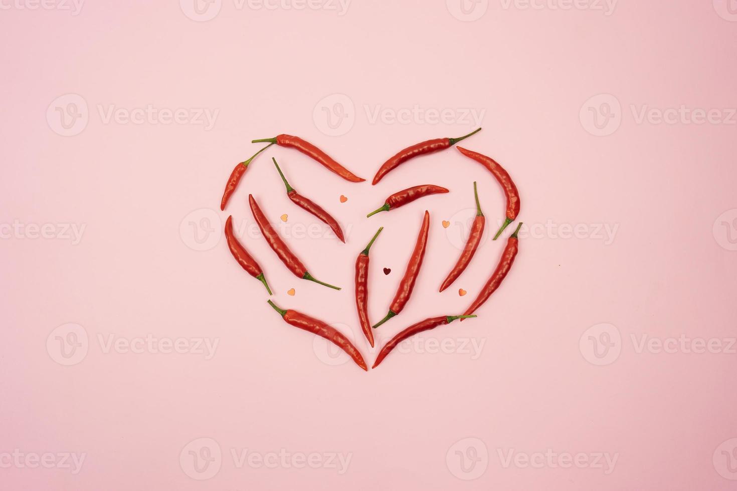 Red hot chilli peppers in the form of the heart lie on a pink background table photo