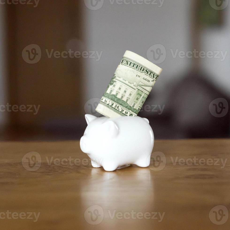 A white piggybank with a dollar banknote inside it stands on a table photo