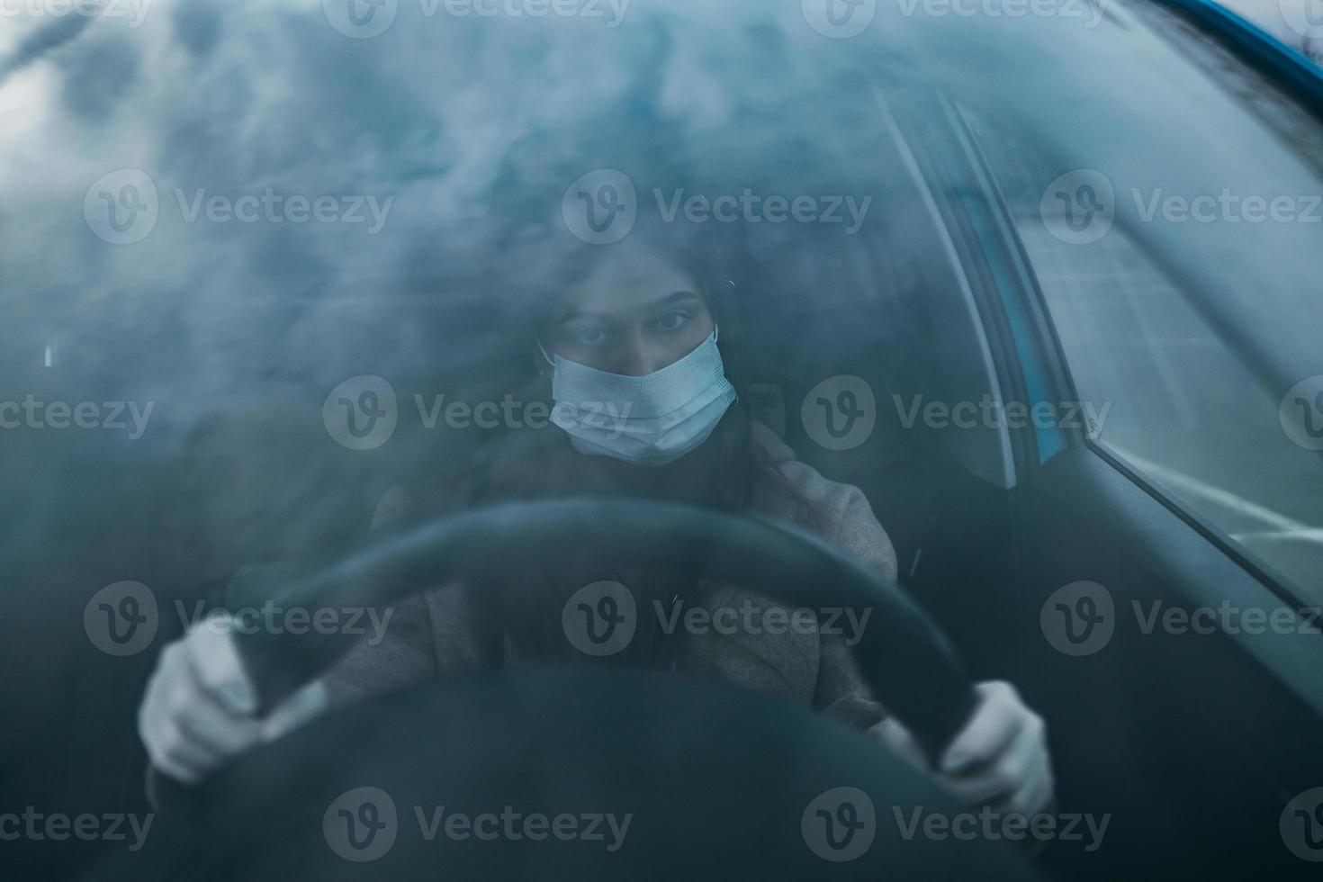 mujer joven con una máscara y guantes conduciendo un automóvil. foto