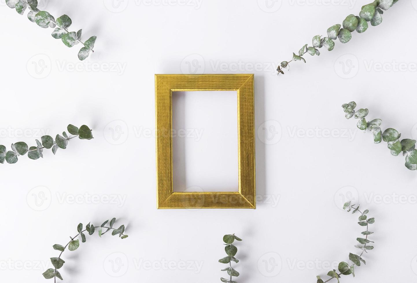 A golden frame for copy space and green leaves of eucalyptus around on a white background. Copy space photo