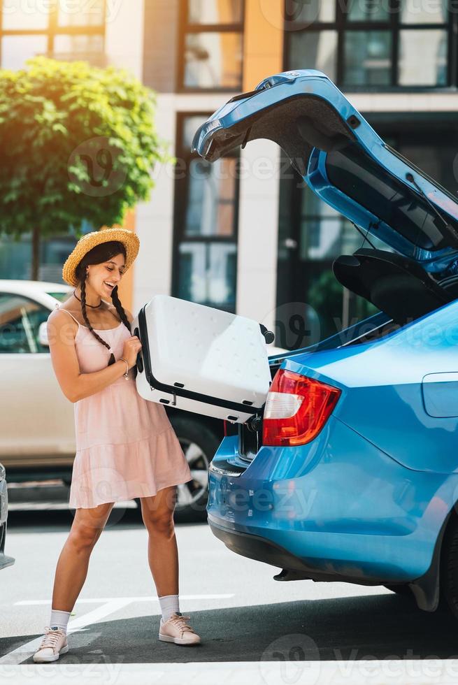 Woman packing her suitcase into luggage boot of the car. photo