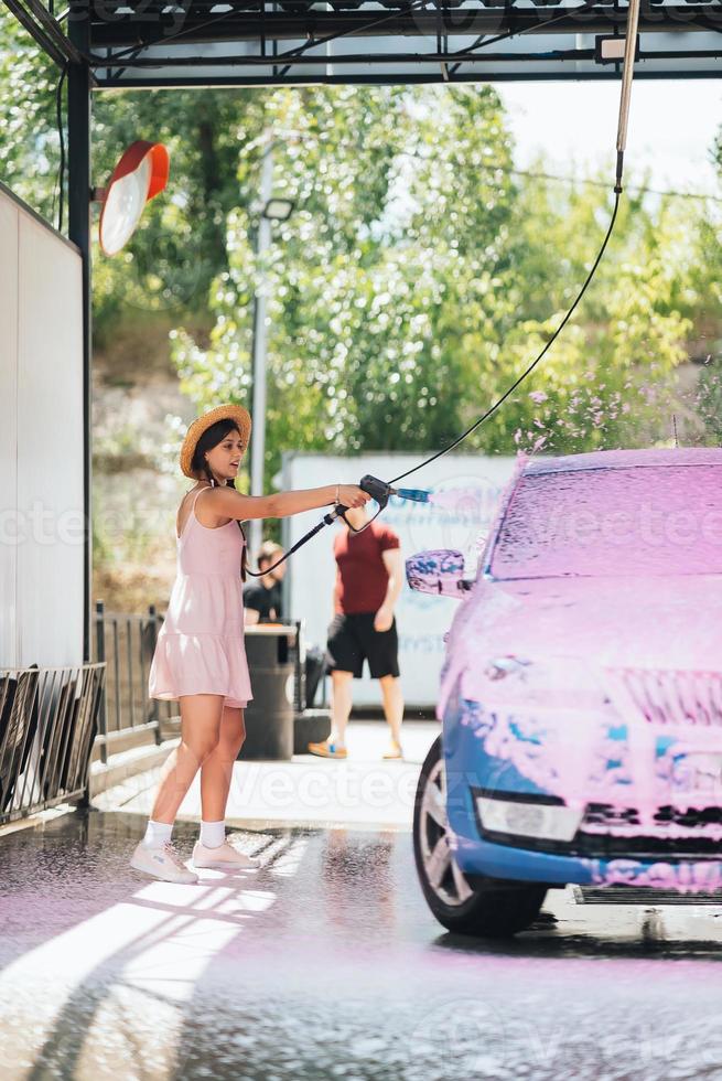 Brunette from a high-pressure hose applies a cleaner on the car photo