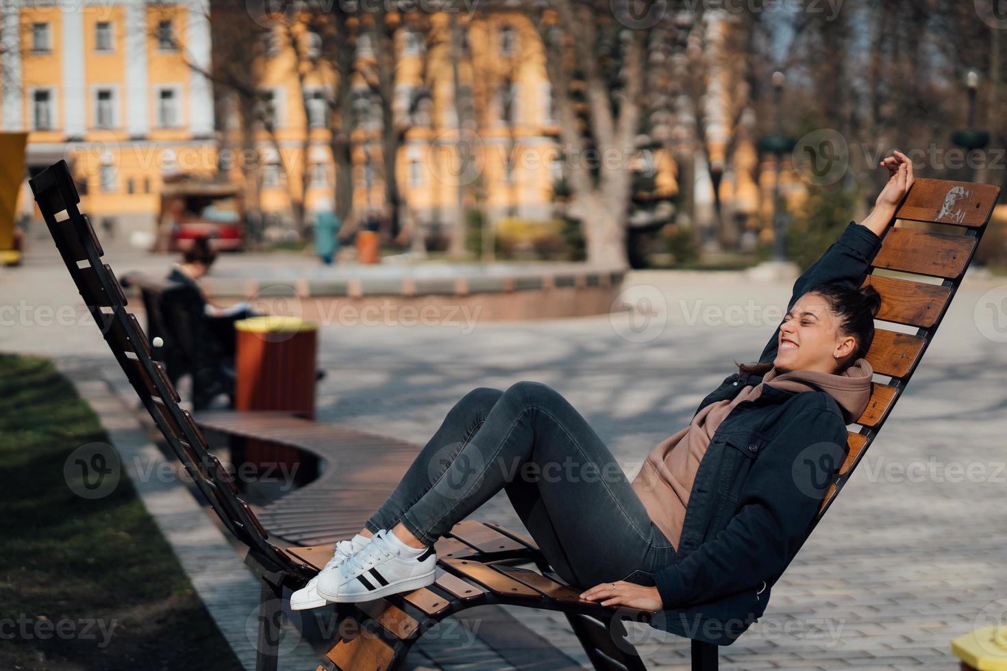 young woman sitting on bench in park, smiling and looking into the camera photo