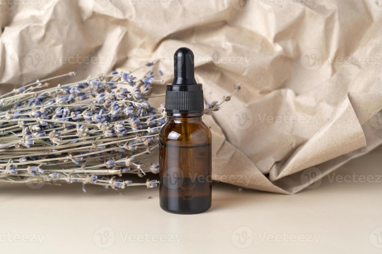 A face serum or oil in a brown dropper bottle standing on a beige table background with lavender flowers nearby photo