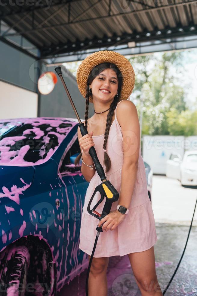 Woman with hose stands by car covered in pink foam photo