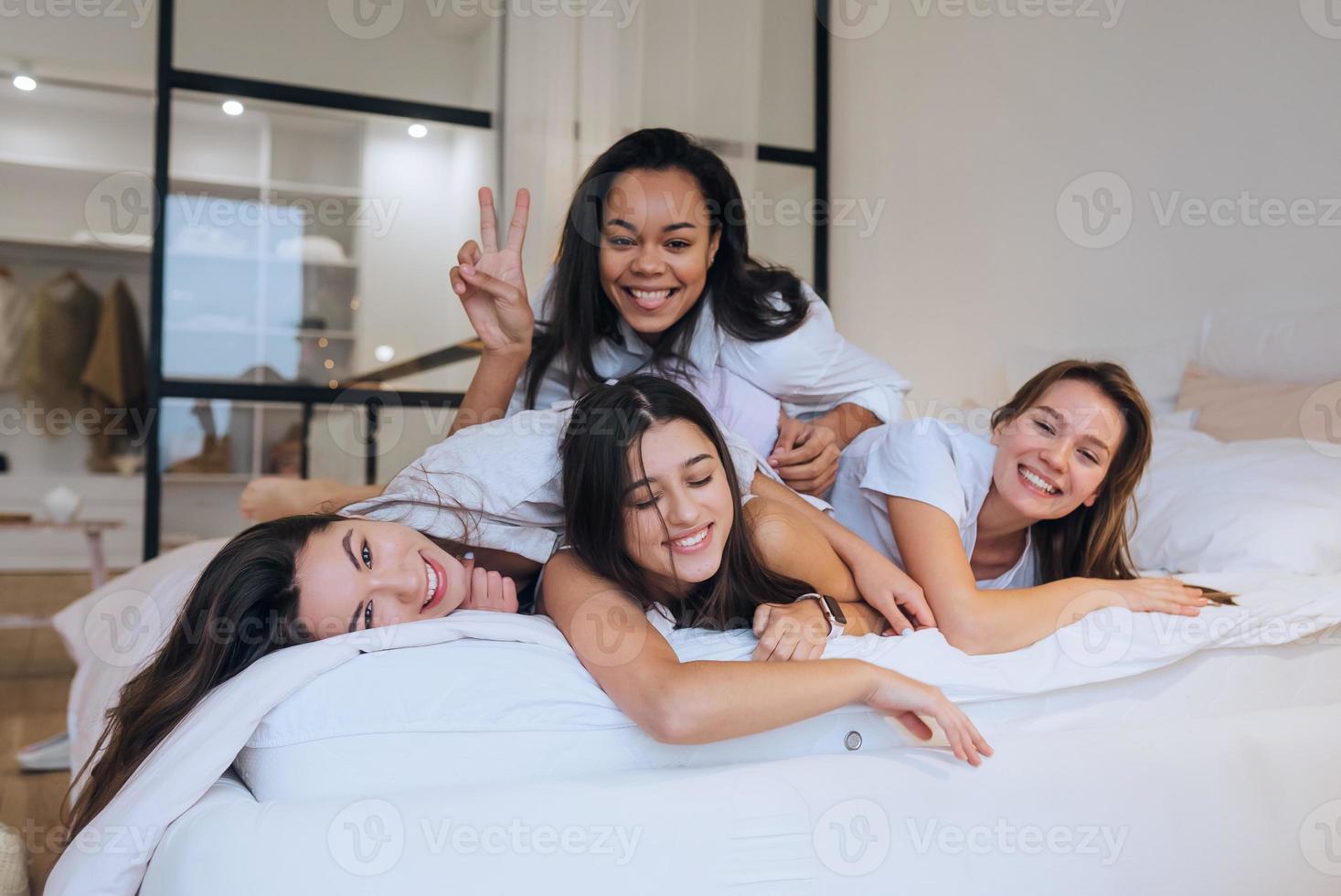 Positive young girls women friends indoors on bed at the hen party at home. photo