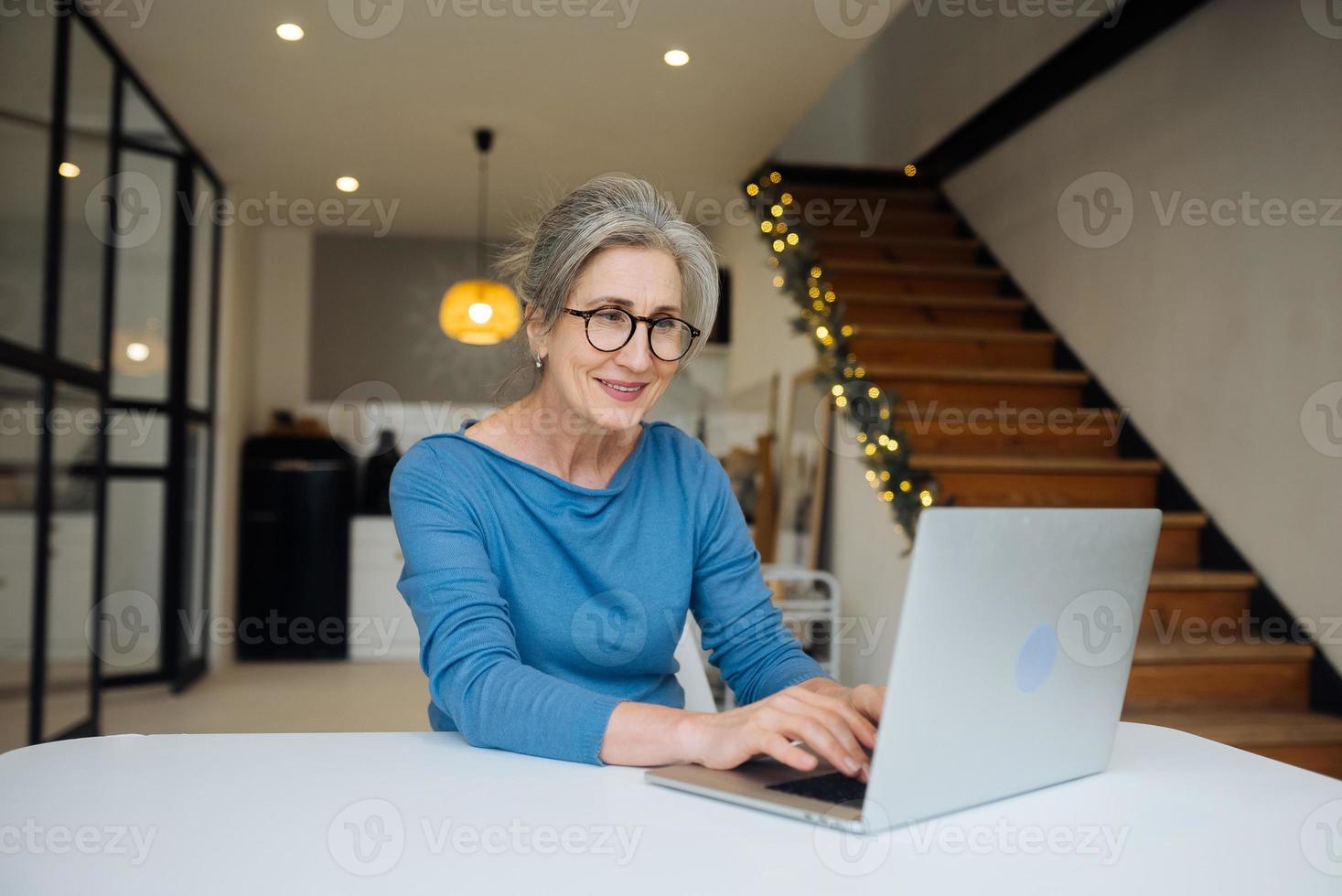 Happy mature middle aged elderly woman looking at laptop photo