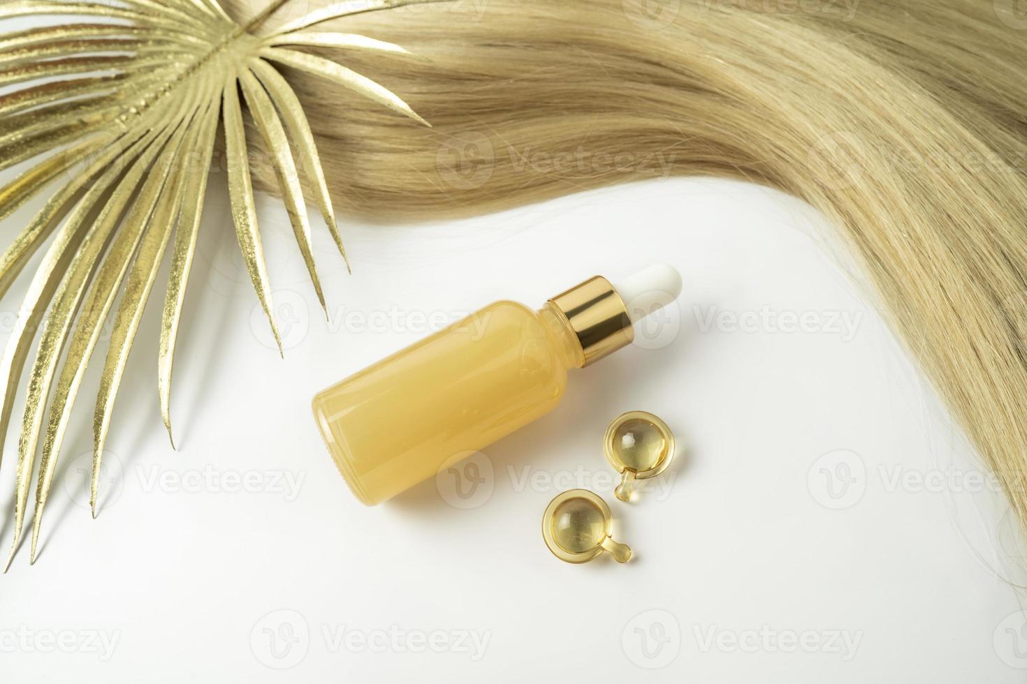 A natural oil or serum for hair care and a ply of blonde hair lying on a white background photo