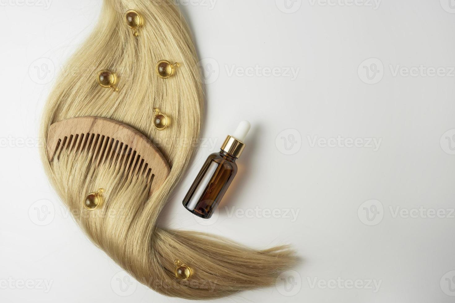 A natural essential oil or serum for hair care in golden capsules lying on a strand of  blonde hair. Hair care and smoothing concept photo