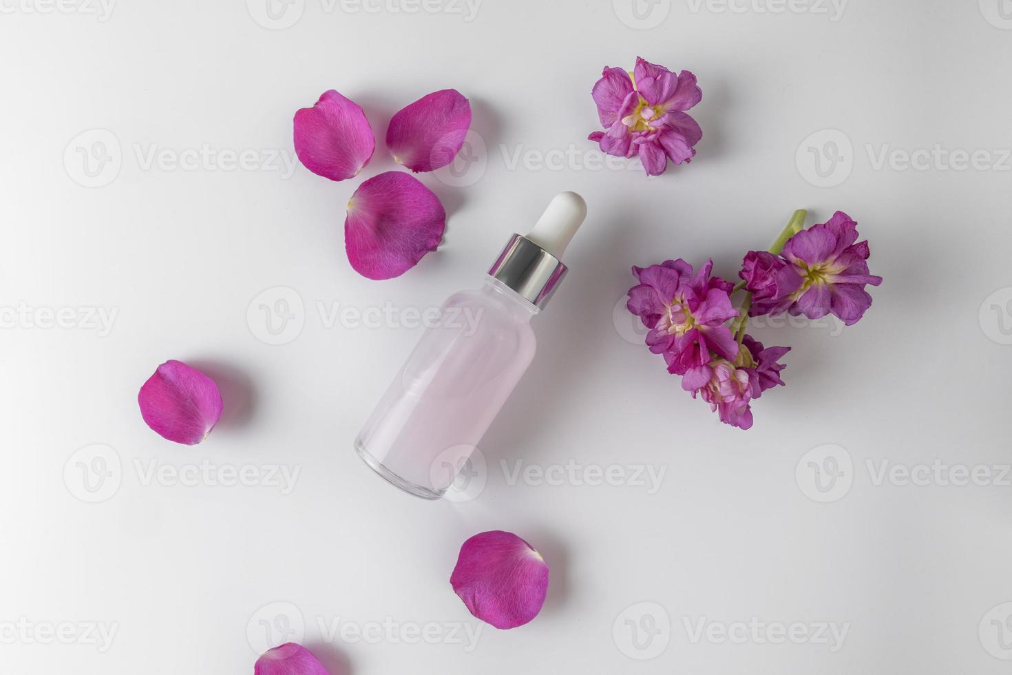 A pink face serum or oil made of rose petals with flower extract lying between the petals, product marketing mockup. A concept of hair care in a salon or at home photo